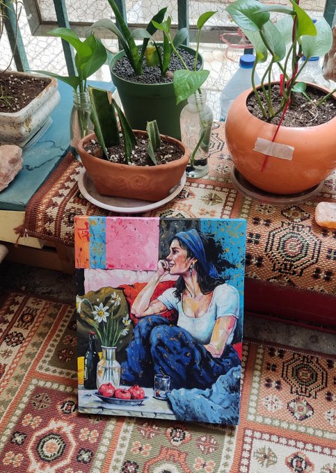 A small still-life painting of a woman in a blue dress, a vase of white flowers, and pomegranates rests on a patterned rug surrounded by potted plants.