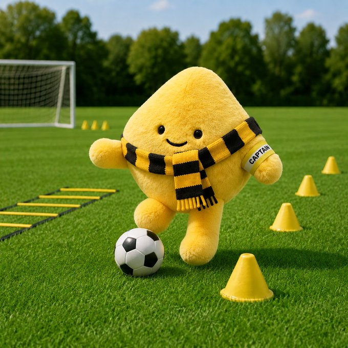 The image features a yellow stuffed animal figure dressed as a soccer player, standing on a grassy field with cones set up around it. The caption of the image includes a reference to the Binance community and a hashtag related to the post "CAPTAINBIBI IS LIVE ON BSC! The captain has arrived Join the movement, unite the Binance community, and be part of the winning team!".