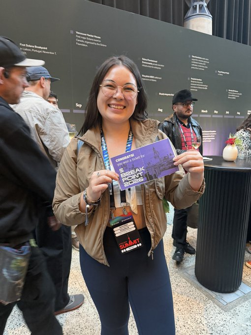 A smiling woman with glasses holds a purple SXSW event badge that reads 'Breakpoint 2023' at what appears to be a conference venue.