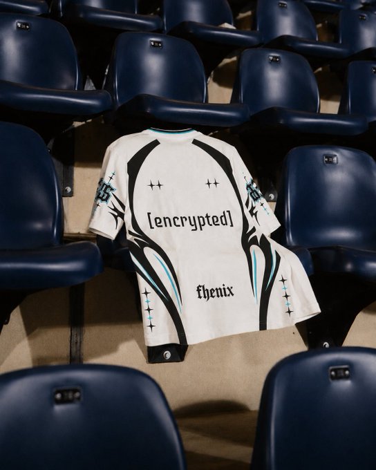 A white esports jersey with black tribal-style graphics and the text '[encrypted]' and 'fenix' is draped over a seat in dark blue stadium chairs.