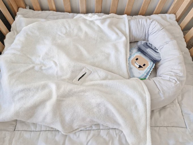 A baby sleeping in a crib, swaddled in a white blanket, with a small plush owl toy beside them.