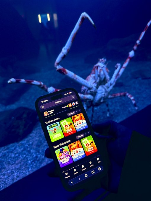 A hand holds a smartphone displaying the "Toshi.bet" app with "SUI" featured prominently under "New Releases" and "Todays Dojos," while a large crab-shaped aquarium decoration glows in the background, tying into the post's promotion of the SUI token on the toshi.bet platform.