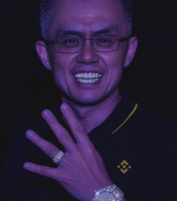 A digitally altered portrait of a man with purple-tinted skin wearing glasses, a black shirt with a yellow stripe, a large diamond-encrusted ring and bracelet, and a grill with diamonds on his teeth, set against a dark background.
