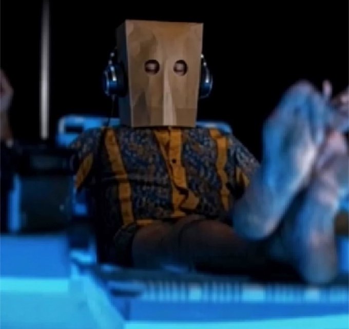 A person with a brown paper bag over their head and headphones on reclines with their feet up, embodying the "anonymous cat" persona referenced in the post about re-entering a Solana memecoin position.
