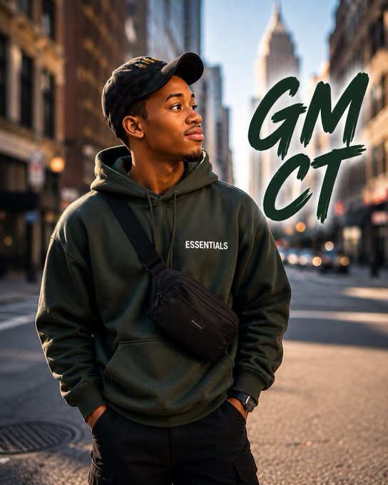 A young man in an olive green Essentials hoodie, black cap, and crossbody bag stands on a city street looking off to the side, with stylized 'GM CT' text in green brushstroke letters.