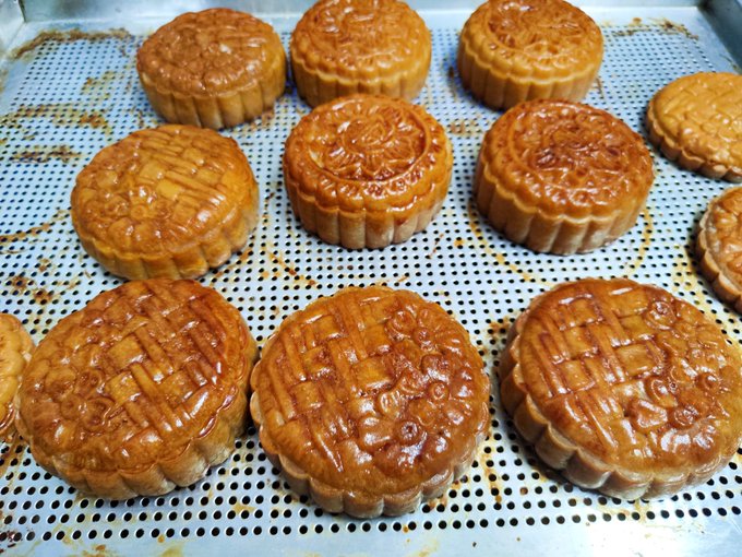 A tray of freshly baked traditional mooncakes with intricate decorative patterns on top is displayed on a metal cooling rack.
