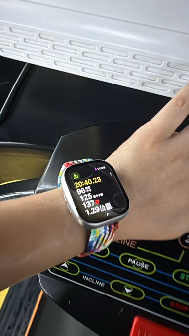 A wrist wearing a multicolored braided band smartwatch displaying a workout summary of 20:40:23 duration, 96 calories, 125 average heart rate, 137 max heart rate, and 1.29 km distance. The person appears to be finishing their gym session on a treadmill, matching the post's mention of a 30-minute incline workout and 1 hour back training.