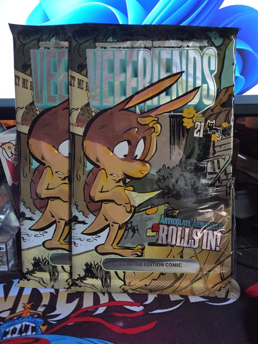A comic book titled "VEE FRIENDS" Issue 21 with the tagline "ARTICULATE ARMADILLO - ROLLS IN!" is displayed as a Limited Edition Comic, featuring a cartoon armadillo character on the cover.