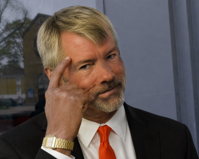 The image features a man dressed formally in a suit and tie with his hand up to his head. The caption of the photo reads "So apparently Saylor sold the bottom to dump Bitcoin even harder just to buy back $100,000,000 for a cheaper price". This implies that the man is involved in cryptocurrency or investing in Bitcoins and has made some sort of financial decision related to the digital currency market.