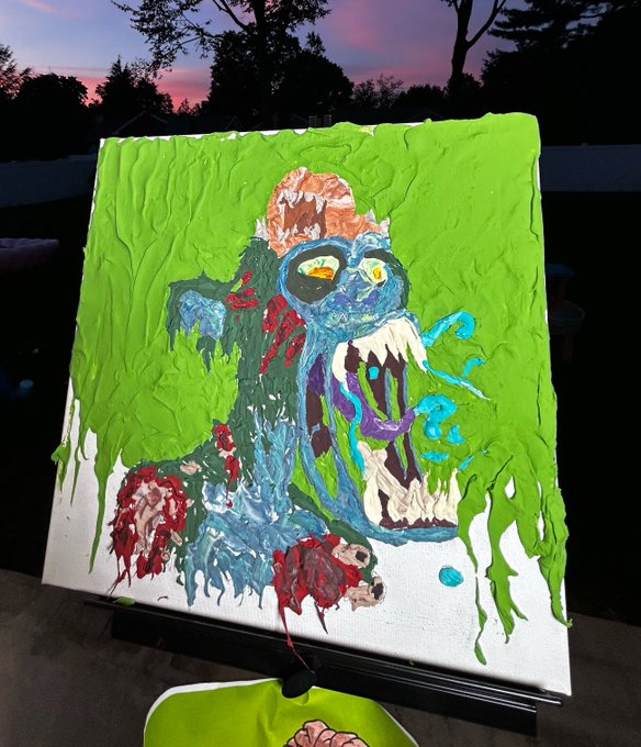 A textured oil painting on a small canvas depicting a monstrous blue creature with sharp teeth and a green background, displayed on an easel outdoors at dusk.