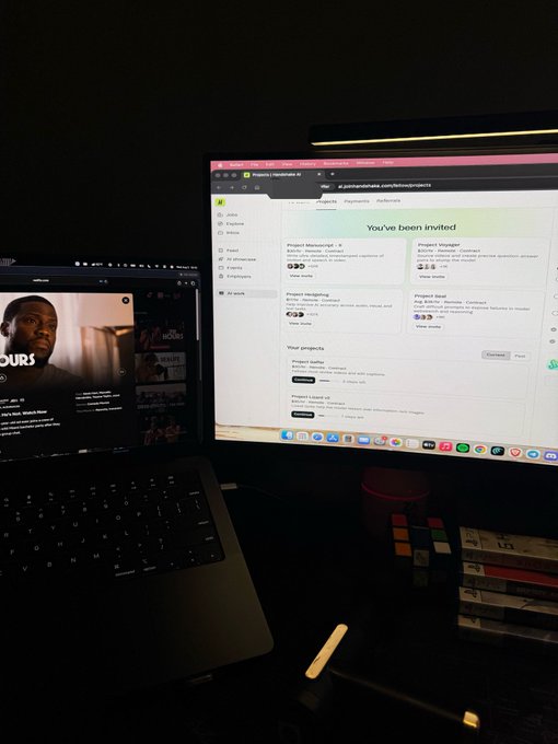 A dimly lit workspace featuring a laptop displaying a video call alongside a desktop monitor showing a Pangea/MakeLab dashboard with the text 'You've been invited' listing project opportunities.