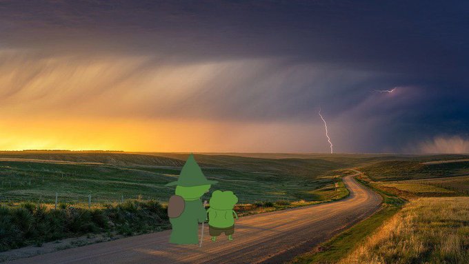 A landscape photo of a dirt road through green hills at sunset with dramatic clouds and a lightning strike, overlaid with a cartoon green character and a smaller green figure standing on the road.