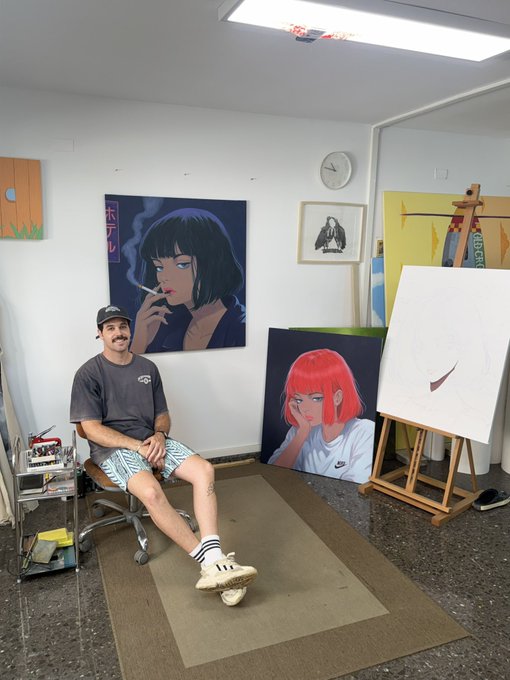The image features a man sitting on a chair, posing for a photo with his legs crossed. He is wearing a gray shirt and white shorts. In front of him are several paintings displayed on the walls, including one depicting a woman smoking a cigarette. The room also has a clock hanging on the wall above the paintings.