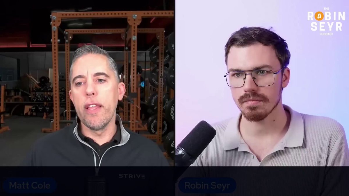 The image shows two men talking into a microphone during an interview or discussion. One man has glasses, while the other has a beard. The background features a gym setting with various exercise equipment visible behind them. The caption of the image reads "Perfect explanation on the relationship between Digital Credit, Bitcoin & Equity".