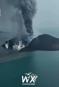 An aerial view of a volcanic eruption producing a large ash plume over water, with a 'WX CHASING' logo at the bottom.