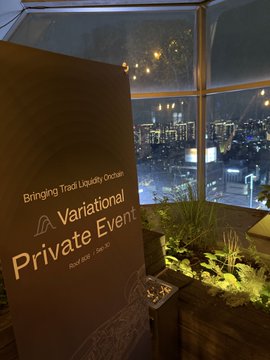 A sign reads "Bringing TradFi Liquidity Onchain Variational Private Event" with a rooftop city view visible through the window behind it.
