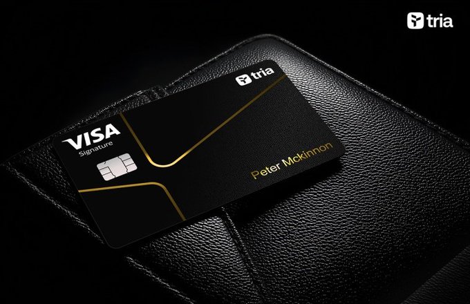 The image features a black wallet with a Visa signature card inside of it. The wallet has a gold stripe running down its center, adding an elegant touch to its design. The card itself is black with a gold stripe running through the middle, making it stand out against the wallet's dark background. The wallet and card are placed on top of a leather purse or wallet case, which is resting on a chair.