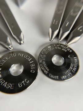 A close-up photograph of two metal stamping dies engraved with text including 'MOLIBD', 'BTC', '3420', '.9999 FINE SILVER', and 'SOLID' arranged on a white surface.