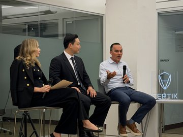 Three people sit on stools holding microphones at a panel discussion, with a 'CERTIK' sign visible on the right side of the stage.