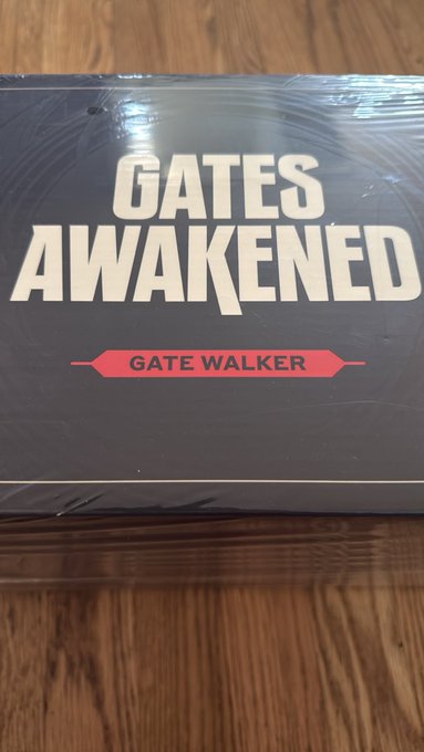 A shrink-wrapped copy of the book 'GATES AWAKENED' by Gate Walker sitting on a wooden surface.