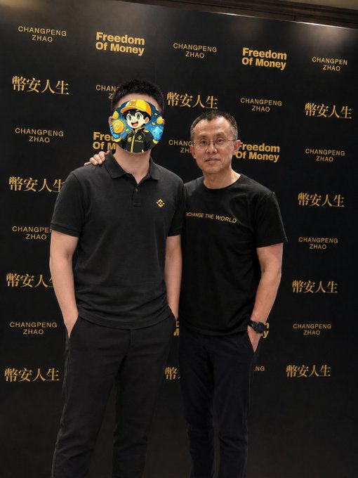 Two men pose together in front of a black backdrop branded with "CHANGPENG ZHAO," "Freedom Of Money," and "幣安人生" (Binance Life), with the taller man's face obscured by a Binance mascot sticker. The man on the right is Changpeng Zhao (CZ), the former CEO of Binance, who is referred to as an "idol" in the accompanying post, where the poster expresses admiration for meeting his hero and compares him to a "majestic lion."