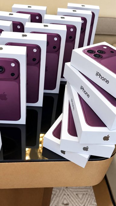 Multiple purple iPhone boxes stacked in a cardboard box, appearing to be a bulk shipment or retail inventory of iPhones.