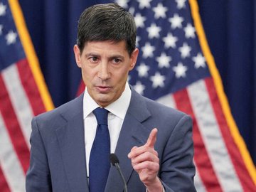 A man in a suit gestures with his hand raised in front of a backdrop featuring multiple American flags, suggesting a formal political or press setting. The image's serious tone mirrors the accompanying post's caution about CPI inflation data potentially causing high volatility in Bitcoin ($BTC), reinforcing the message to be careful and patient with trades.