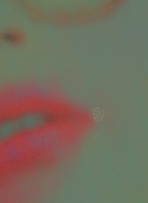 Heavily blurred abstract image with indistinct red, orange, and gray shapes against a greenish-gray background.