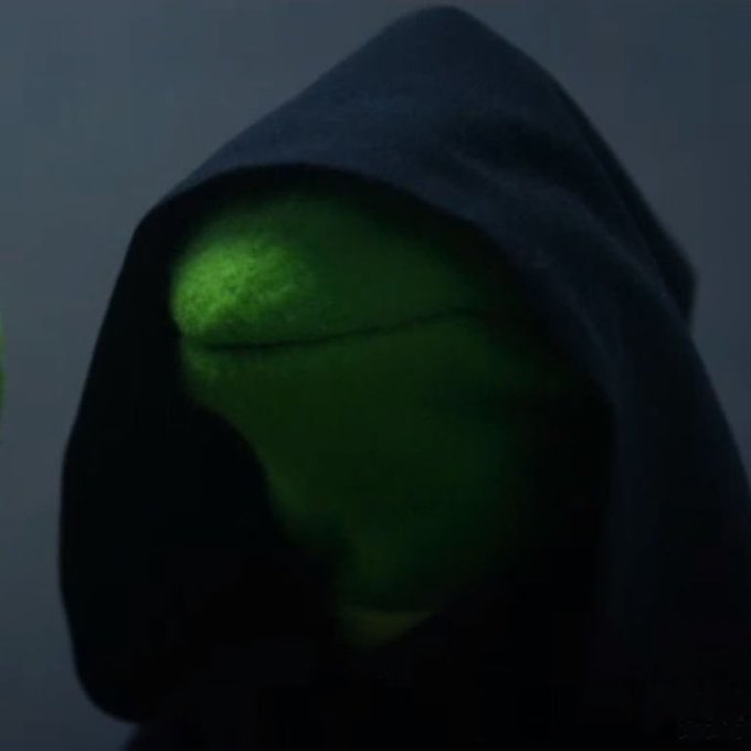 A green frog resembling Kermit the Frog's evil counterpart peeks ominously from beneath a dark hood, paired with a post hyping "$hood" as a newly launched Robinhood meme token positioned to capitalize on the current memestock meta.