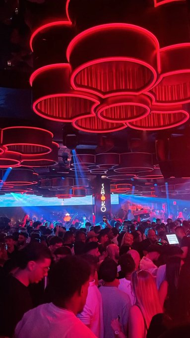 The image shows a crowded nightclub with striking red circular neon lights on the ceiling and a "JANGO" sign visible in the background, perfectly capturing the energetic weekend nightlife vibe to match the "GM" (Good Morning/weekend) post.