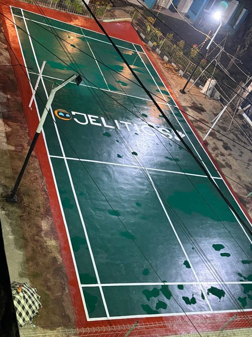 A rain-soaked, empty "JELITICS" branded sports court at night, overlaid with power lines, highlights how the brand's promotional gimmicks mask the real financial losses many crypto gamblers face.