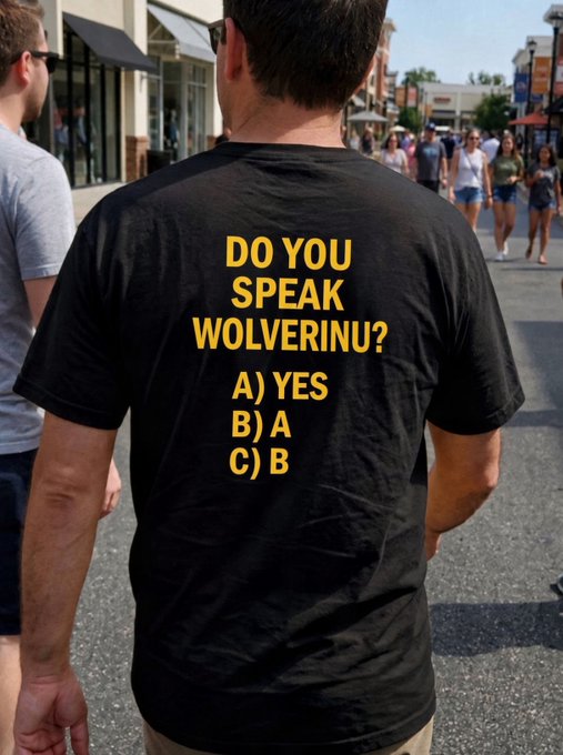 A person walking on a street wearing a black t-shirt with yellow text reading 'DO YOU SPEAK WOLVERINU? A) YES B) A C) B'.