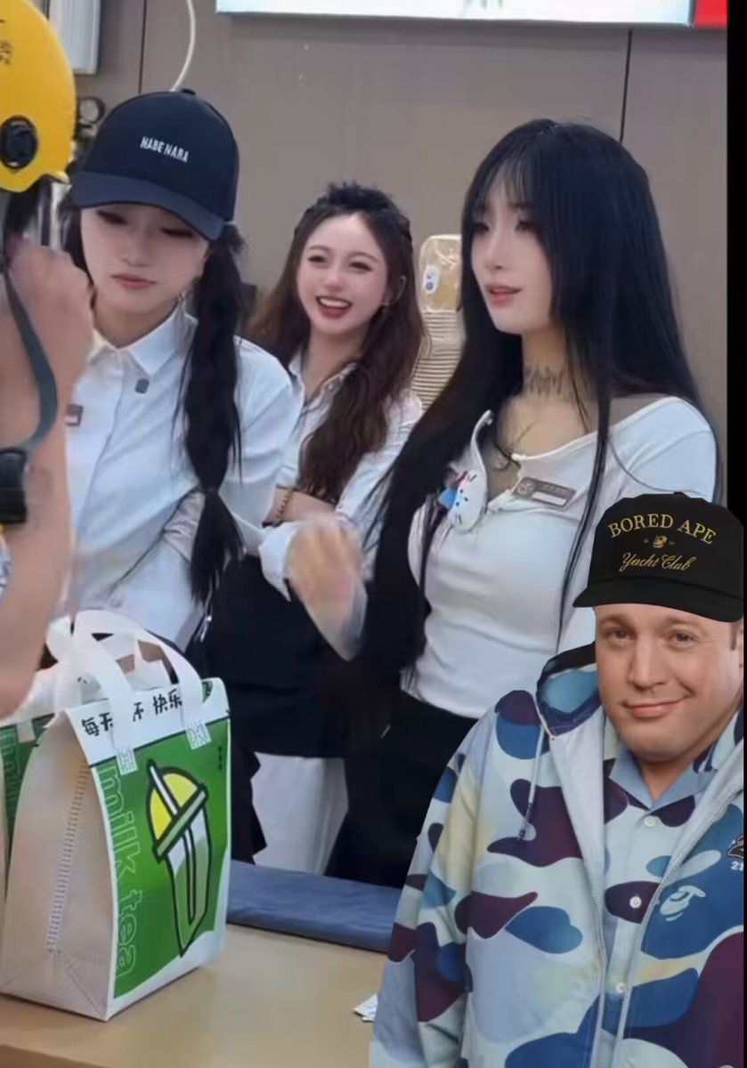 The image shows a group of people, including two women wearing baseball caps with "BAYC" written on them, standing around a table or counter. One woman has her arm around another woman's shoulder while they are all smiling at the camera. A man is also present in the scene, and he appears to be looking at something off-camera. The background of the image features a wall that says "BAYC", which could potentially be related to the content or context of the photo.