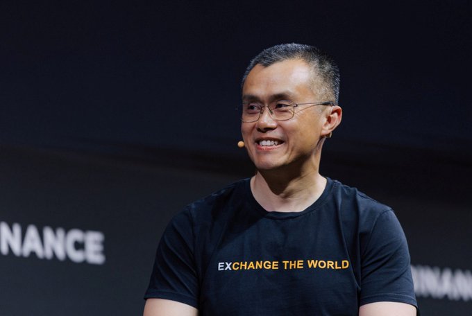 A man wearing glasses and a headset microphone smiles on stage, wearing a black t-shirt that reads "EXCHANGE THE WORLD," with partial "NANCE" text visible in the background referencing Binance. The image relates to the post by showing Big Cousin (cz_binance), the interview subject being discussed, who exemplifies the engineer's mindset the author describes.