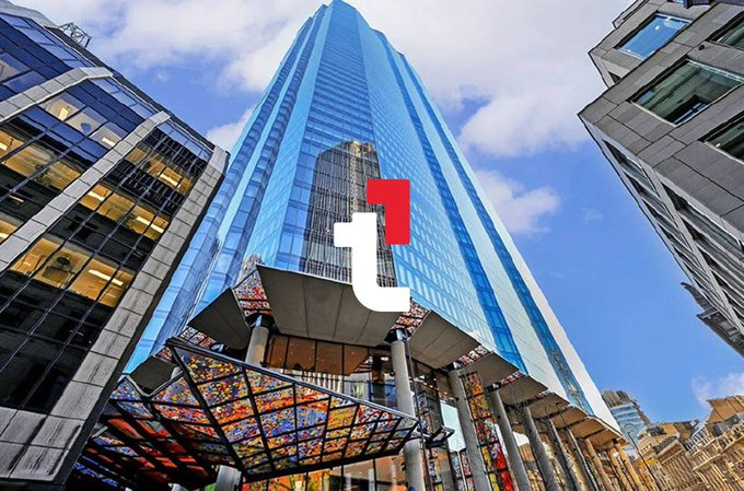 A low-angle photograph of a tall modern glass skyscraper against a partly cloudy sky, featuring a red and white "i" logo overlaid in the center of the image.