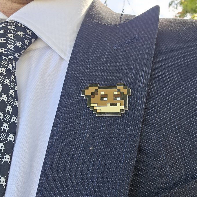 Close-up of a person wearing a navy suit with a pixelated Minecraft dog pin on the lapel.