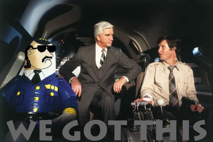 A humorous edit showing two men in suits inside an aircraft cockpit, with an inflatable police officer character seated on the left and 'WE GOT THIS' text overlaid.