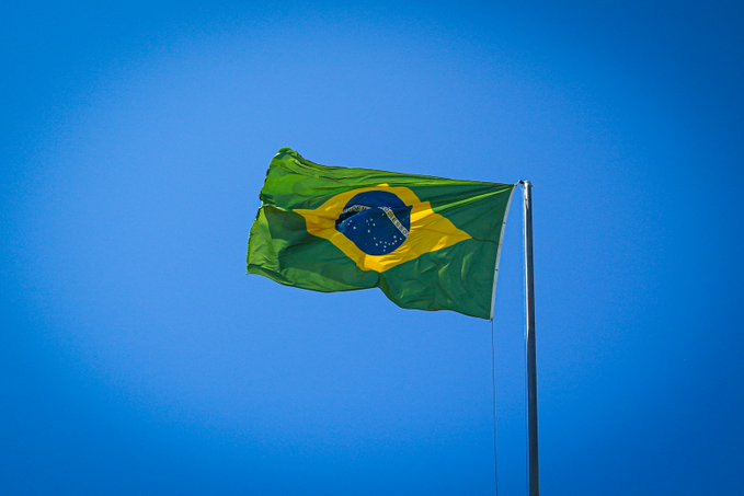 The Brazilian flag waves against a clear blue sky, symbolizing the country's latest regulatory move to classify crypto VASPs alongside securities brokerages under its central bank's framework by 2027.