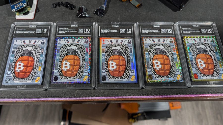 Five graded cryptocurrency-themed trading cards encased in TAG slabs, each featuring a Bitcoin 'B' logo grenade design and labeled 'CRYPTOMAS' with grades of 9 or 10.
