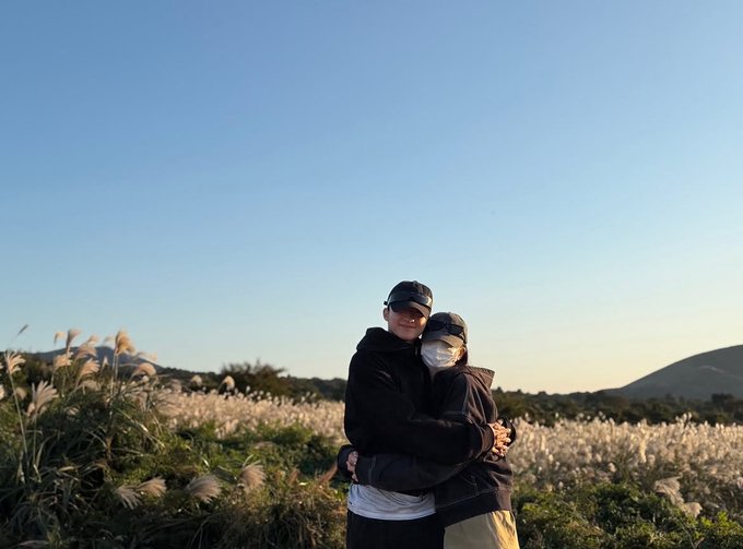 A couple embraces while wearing face masks in a field of tall pampas grass at sunset, humorously captioned "Shiba, seriously lololol."