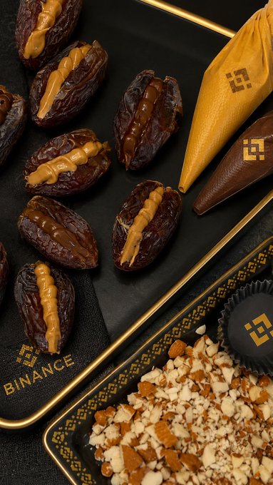 The image showcases dates stuffed with fillings and sprinkles of chopped almonds, with a binance logo subtly featured on the packaging and a wrapper. This directly complements the post's theme of "date sweetness," the "crunch of almonds," and the "golden touch of Binance."