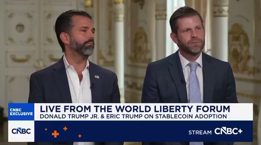 The image features two men dressed in suits, standing next to each other against a brown background. They are positioned behind a podium, which suggests they might be participating in an event or discussion related to the topic of Bitcoin. The text on the image reads "Live from the World Liberty Forum Donald Trump Jr. & Eric Trump on Stablecoin Adoption Stream Cbc+". This indicates that the two men could be discussing the implications and potential impact of Bitcoin adoption, given their roles as a prominent political figure and an expert in the field.
