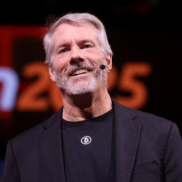 Michael Saylor, Executive Chairman of Strategy (formerly MicroStrategy), smiles on stage at what appears to be a Bitcoin 2025 conference, with the partial "2025" logo visible behind him. The image relates to the post as it shows the key figure discussing how Bitcoin treasury companies like his own Strategy and Strive mutually reinforce one another, citing Strive's $50 million STRC preferred stock purchase as evidence of their collaborative ecosystem.