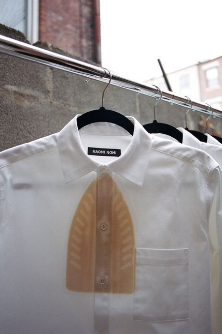 A white button-up shirt on a black hanger displays a graphic print of an open shirt front, with a label reading 'NAOMI NOMI'.