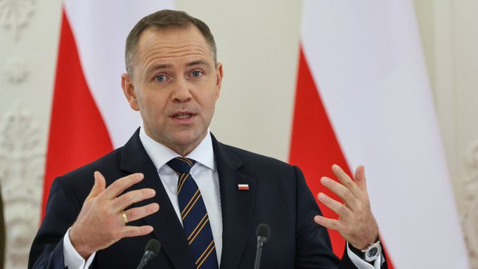 A man in a dark suit and striped tie gestures with both hands while speaking at a podium, with the red and white flag of Poland visible behind him, suggesting he may be a Polish official.

Note: I cannot identify the specific person in the image based on facial features. If you could confirm who this is, I could provide more specific context about how they relate to Poland's decision regarding MiCA implementation and cryptocurrency regulation.