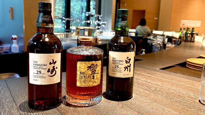 Three premium Japanese whisky bottles—Yamazaki 25, Hibiki 30, and Hakushu 25—displayed on a wooden bar counter.