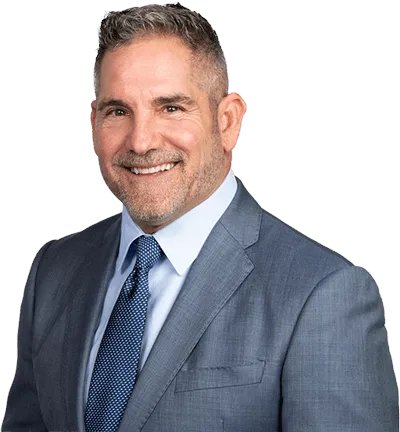 A professional headshot of a smiling middle-aged man with graying hair and a beard, wearing a gray suit, white shirt, and blue patterned tie against a white background.
