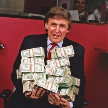 This image features a man dressed in a suit holding a large quantity of cash, with stacks secured by bands across the denominations. The context of the image, combined with the accompanying text "BOOM!", suggests a significant increase or success in a financial endeavor, which could be related to a business, political campaign, or other financial venture. The number of bands or specific denominations are not clearly visible to provide further numerical details.