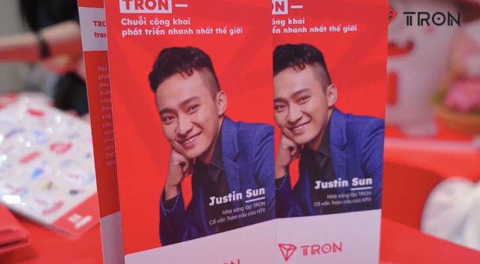 Promotional materials featuring TRON founder Justin Sun are displayed at the Conviction 2026 conference in Ho Chi Minh City, where TRON participated as a Diamond Sponsor. The red brochures showcase Sun's photo alongside the TRON logo and Vietnamese text highlighting TRON's status as the world's fastest-growing public blockchain.