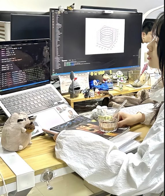 A woman in a white blouse works at a desk with multiple monitors, one displaying a 3D graph and another showing code, while a cat rests nearby and she holds a bubble tea.